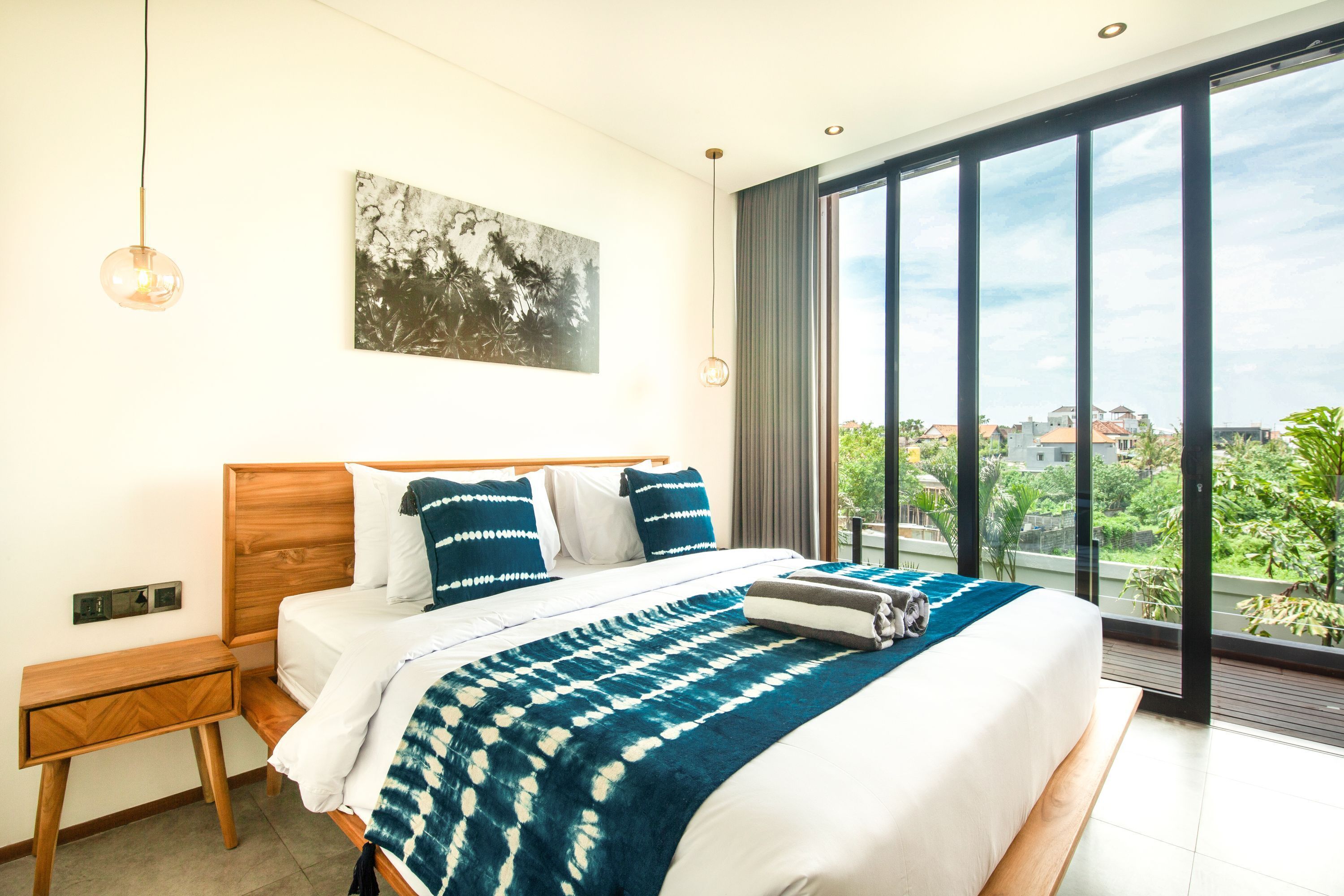 Una camera da letto moderna con un letto grande, un comodino, una lampada a parete e vista sulla città attraverso ampie finestre.