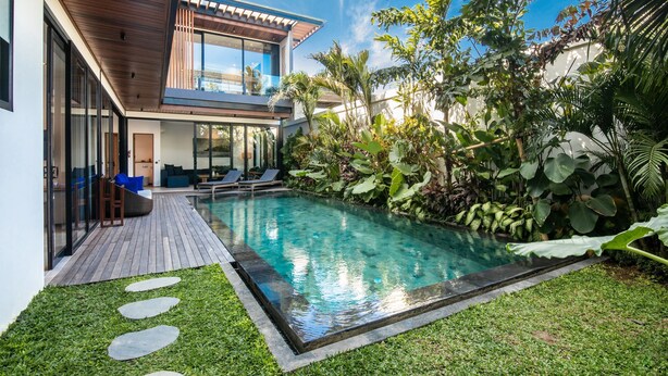 Ein modernes Haus mit Pool, einer Holzterrasse und üppiger Bepflanzung.