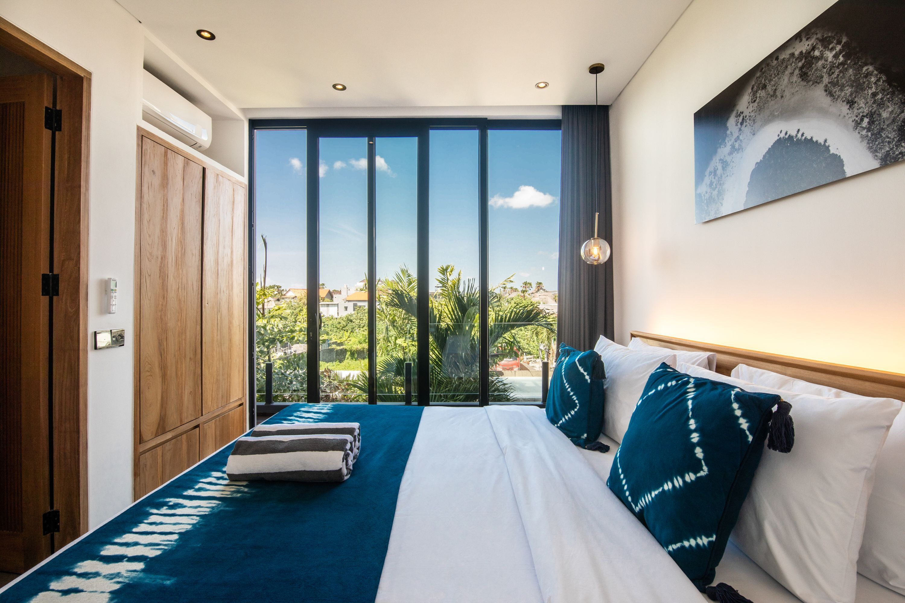 A hotel room with a large bed, a view of greenery and buildings, and a ceiling fan.