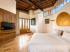 A bedroom with a large bed, a television on a wooden cabinet, a window with curtains, and a ceiling fan.