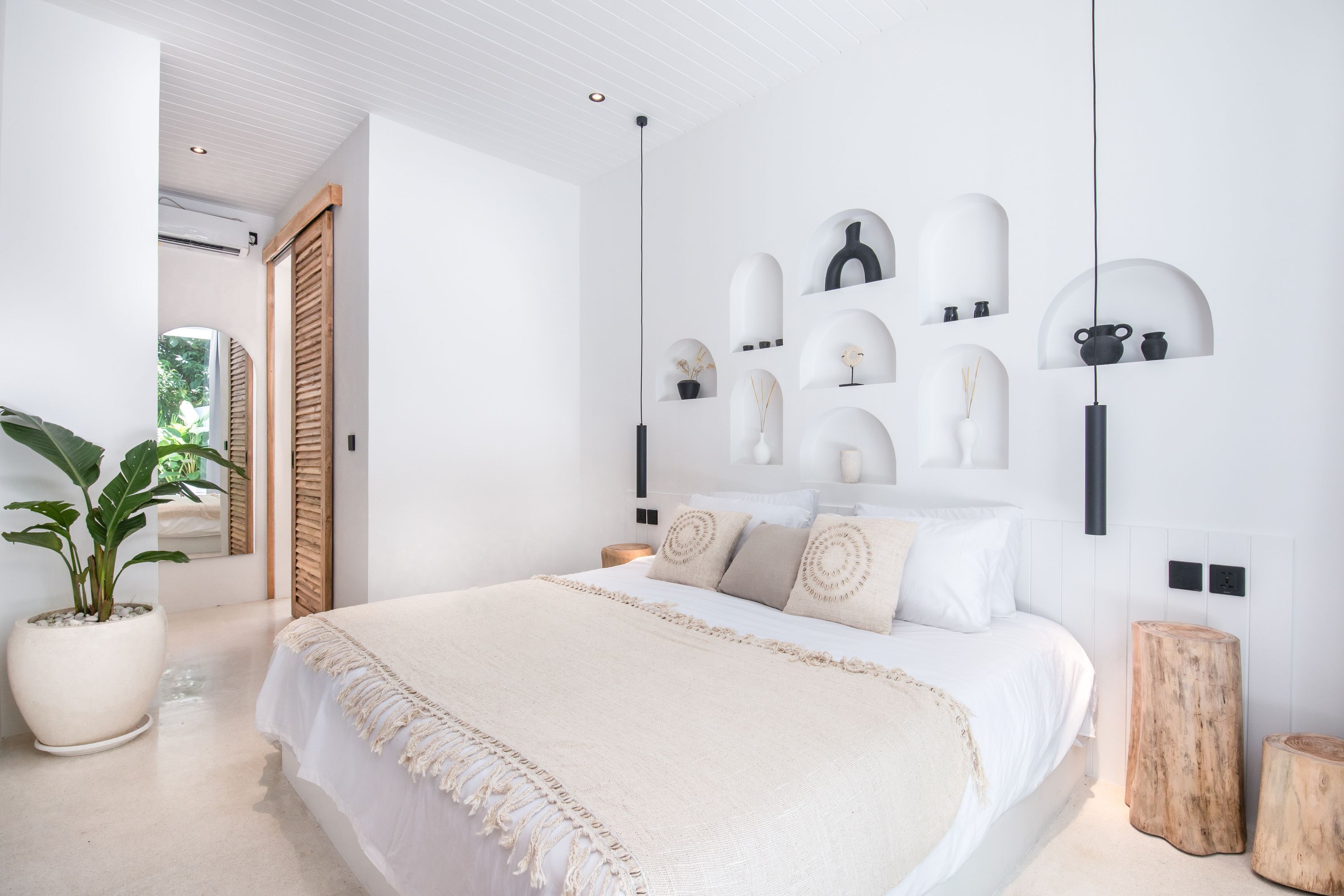 A modern bedroom with a large bed, a potted plant, and a minimalist wall decor.