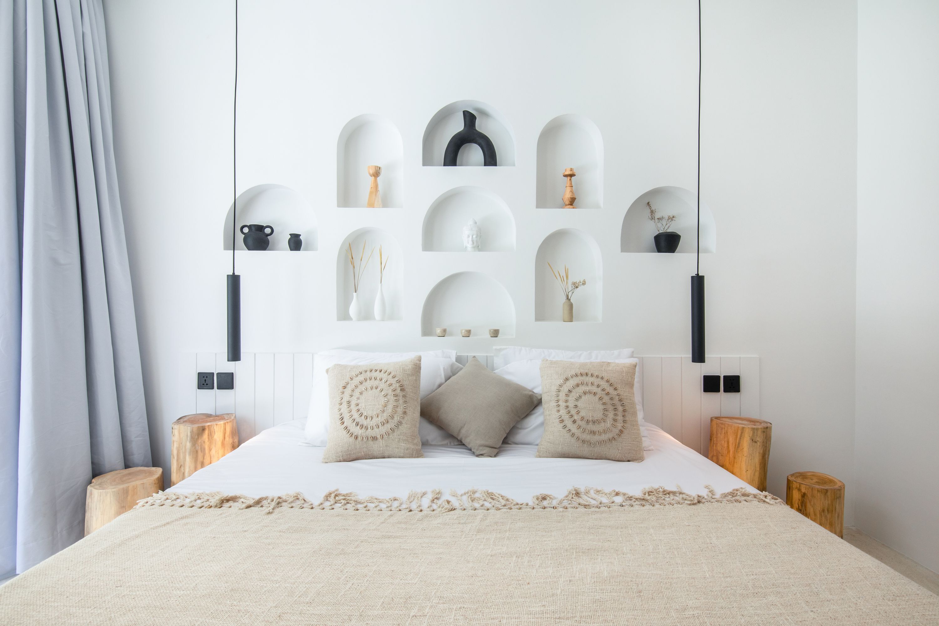 A modern bedroom with a bed centered under a wall-mounted shelf with decorative items.