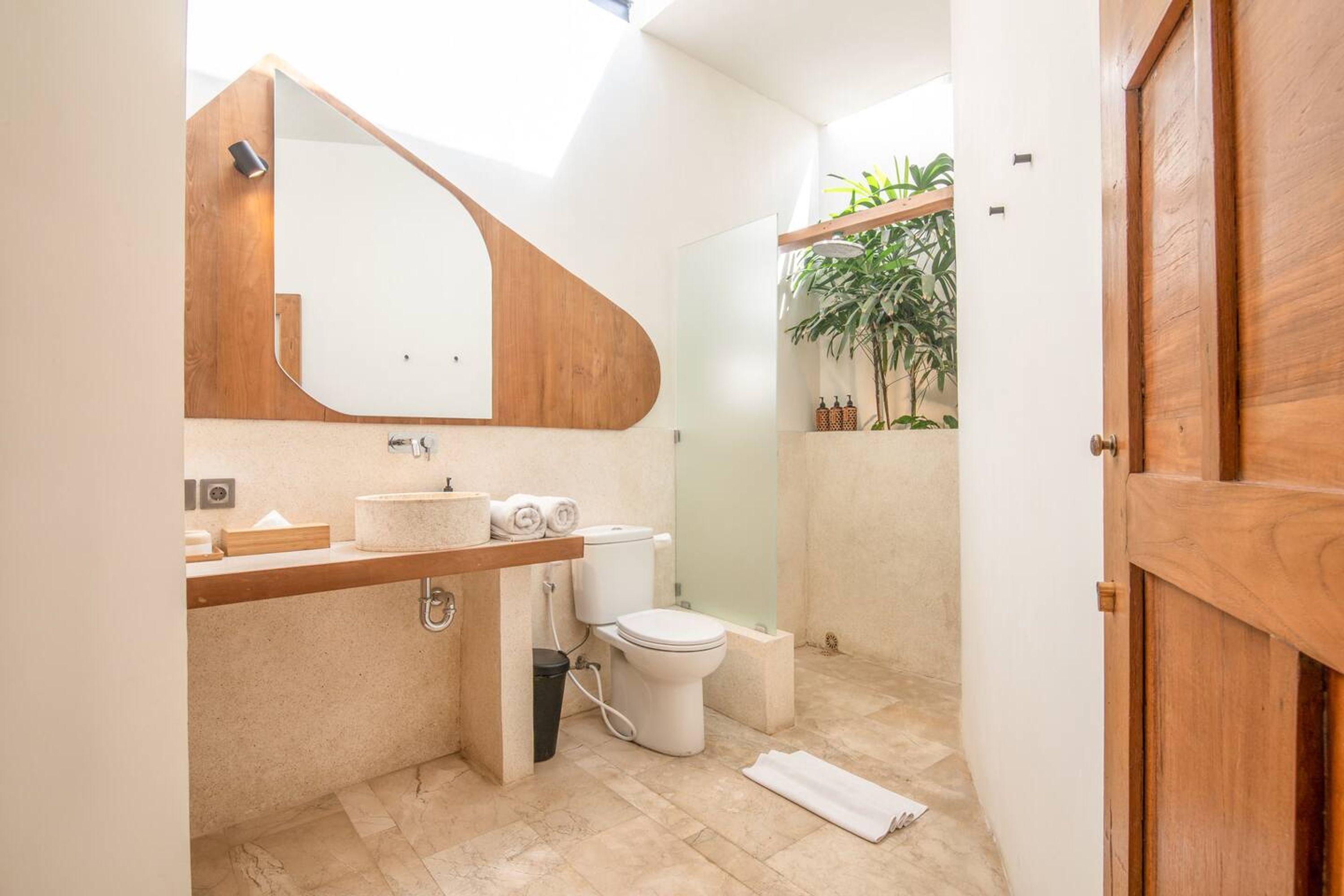 A modern bathroom with a wooden vanity, a large mirror, a toilet, and a shower area.