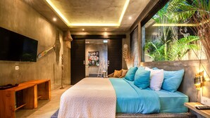 A modern bedroom with a large bed, a TV mounted on the wall, and a window with a view of plants. - Mette 3br Villa in Dalung (Canggu)