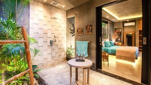 A modern bathroom with a shower, a round table with bottles, and a bed visible through an open door. - Mette 3br Villa in Dalung (Canggu)