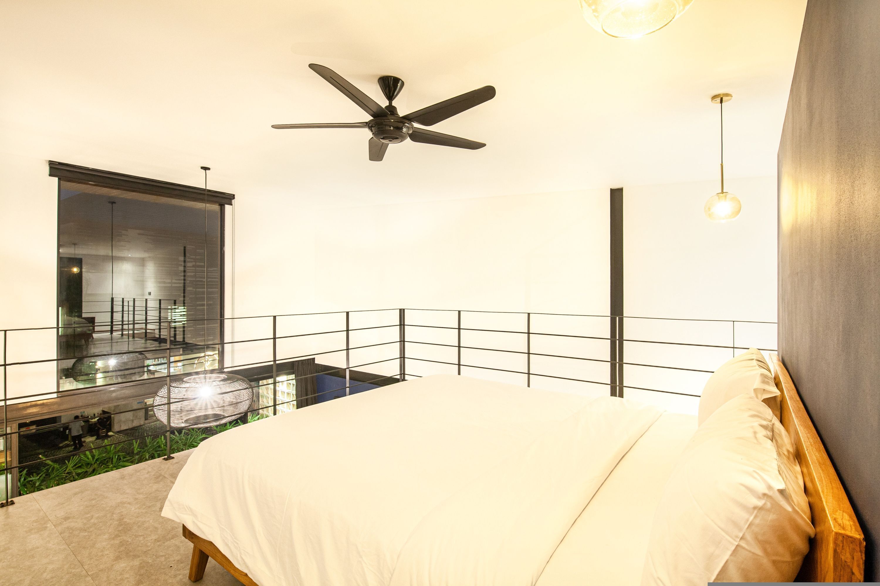 A modern bedroom with a bed, a ceiling fan, and a balcony with a glass barrier.