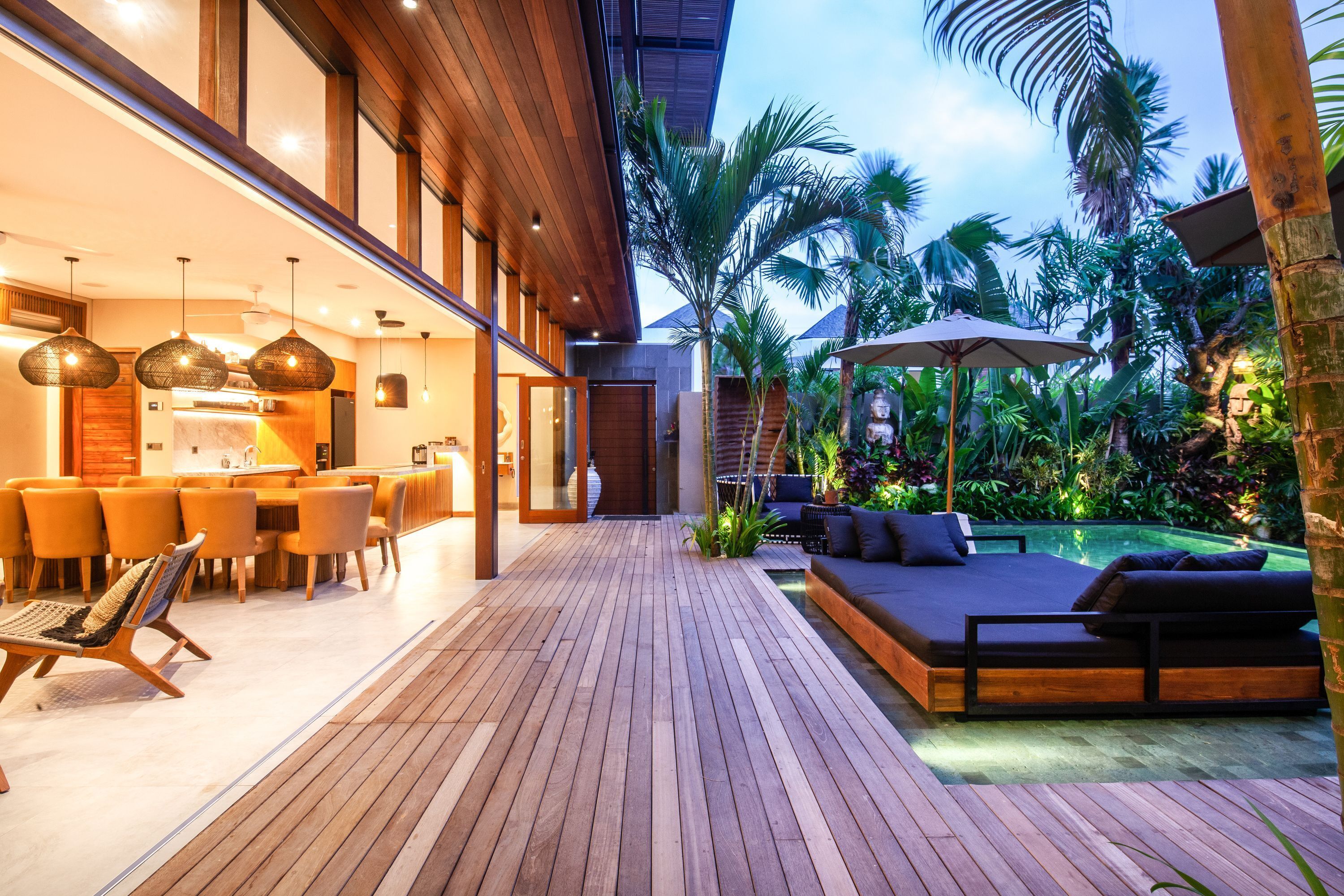 A modern outdoor patio with wooden flooring, a dining area with orange chairs, and a pool area with a lounge chair and umbrella.