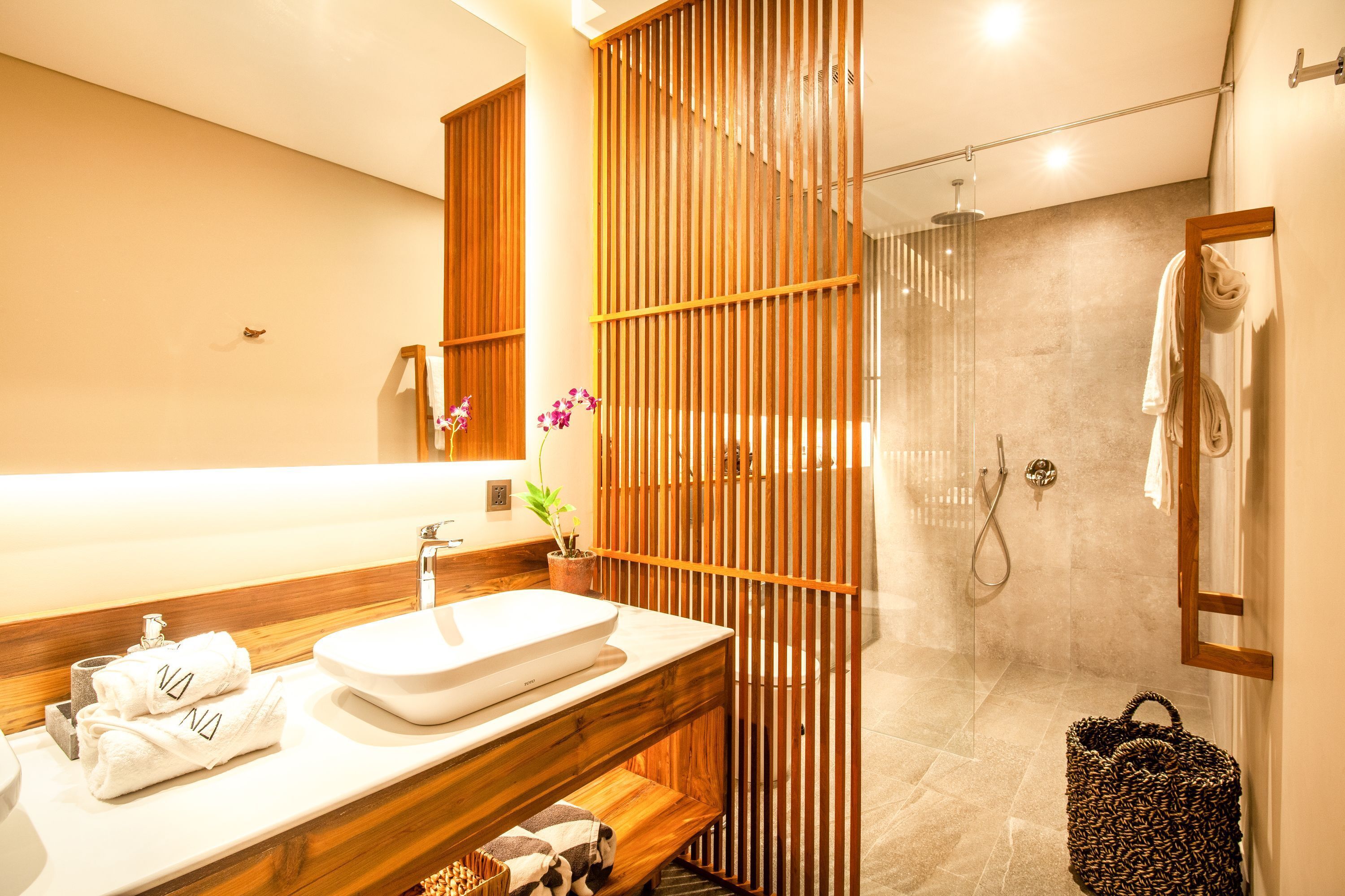 Un baño moderno con tocador de madera, un espejo grande, un lavabo blanco y una ducha con cerramiento de vidrio.