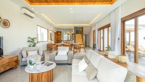 A spacious living area with a wooden ceiling, a dining area, and large windows offering a view of the outdoors. - Breeze Opulent 6 BR in With Ocean View 5 Mins to Savaya (Pecatu)