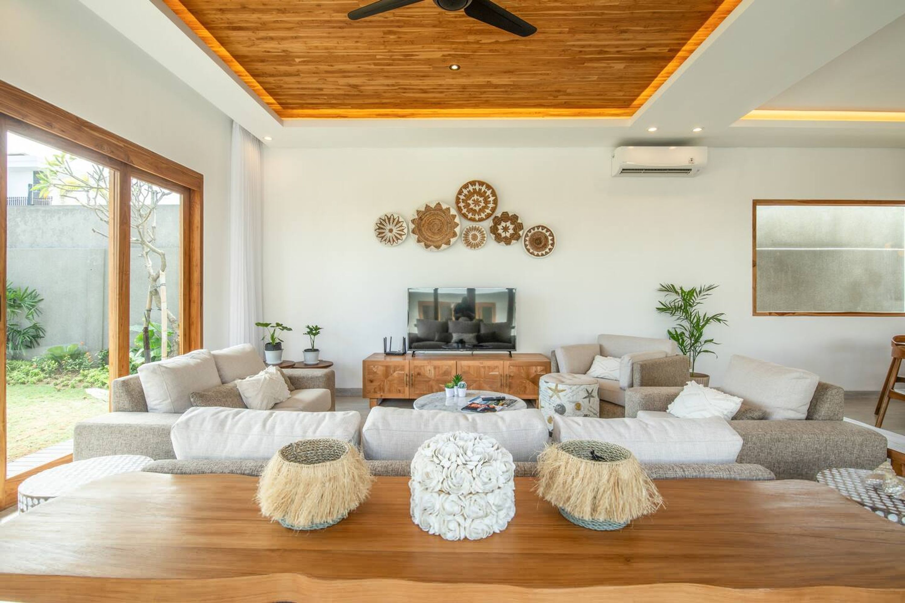 A modern living room with a wooden ceiling, a large TV, and a sofa set.