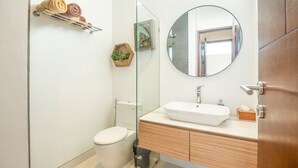 A modern bathroom with a glass shower enclosure, a round mirror, and a wooden vanity. - Mateo Villa Marvelous 6BR 2 Mins to Beach (Tibubeneng)