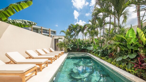 A poolside area with lounge chairs and a clear pool, surrounded by tropical plants and palm trees. - Mateo Villa Marvelous 6BR 2 Mins to Beach (Tibubeneng)