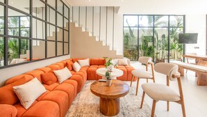 A modern living room with a large orange sectional sofa, a round wooden coffee table, and a dining area with a wooden table and chairs. - Mateo Villa Marvelous 6BR 2 Mins to Beach (Tibubeneng)