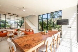 Amplia sala de estar con un gran comedor de madera, sillas blancas y una escalera moderna.