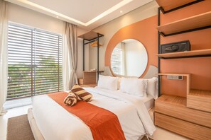A modern hotel room with a large bed, a wooden nightstand, a round mirror, and a view of greenery through the window.