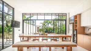A modern kitchen with a large dining table, wooden cabinets, and a TV. - Mateo Villa Marvelous 6BR 2 Mins to Beach (Tibubeneng)