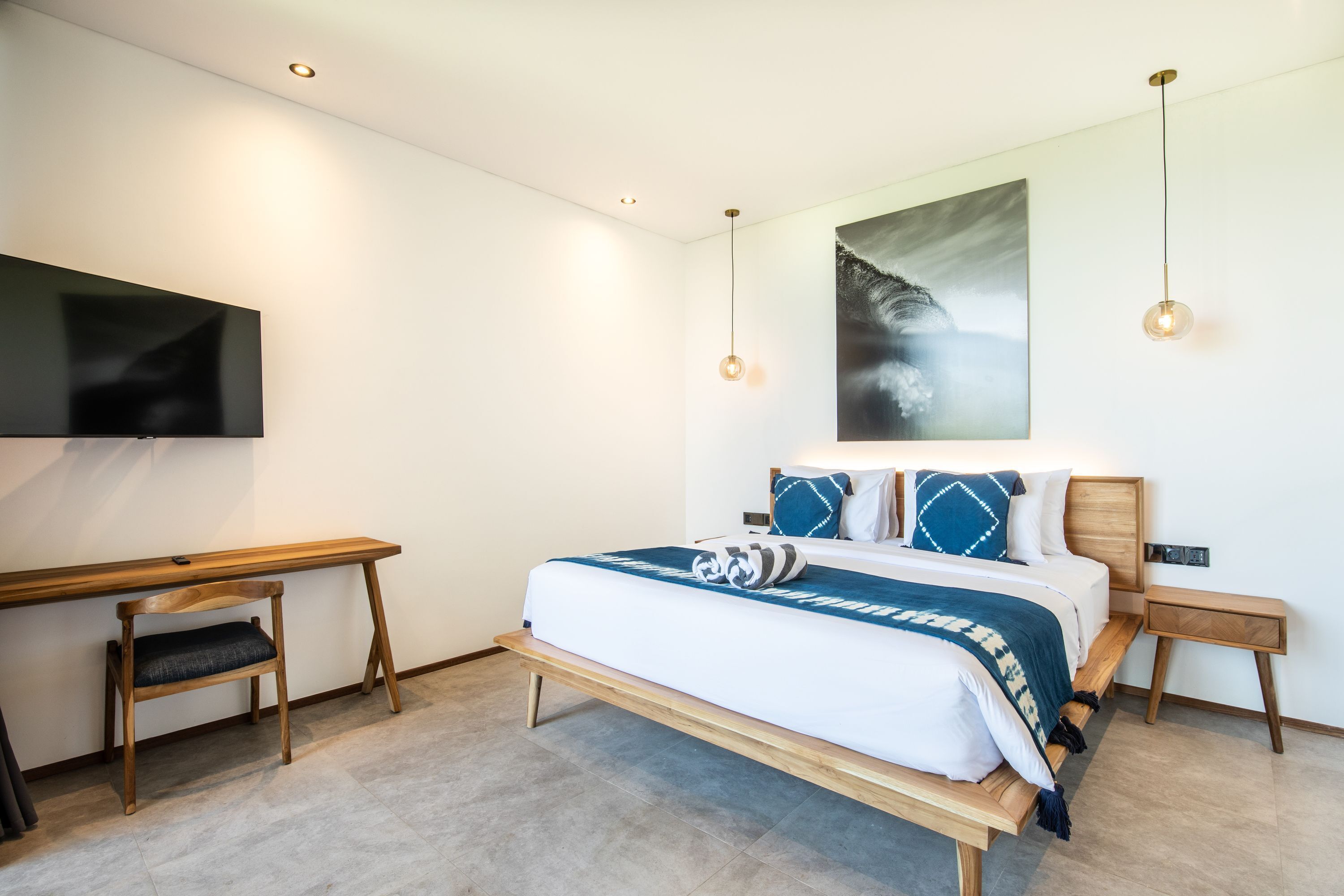 A modern bedroom with a wooden bed, a desk, and a TV mounted on the wall.