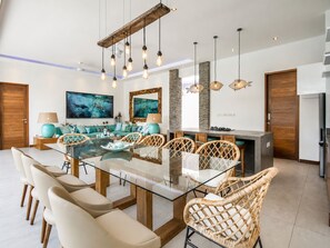 A modern kitchen with a central island, a dining area with a glass-top table, and a living space with a sofa and artwork. - Marina Villa in Seminyak (Seminyak)