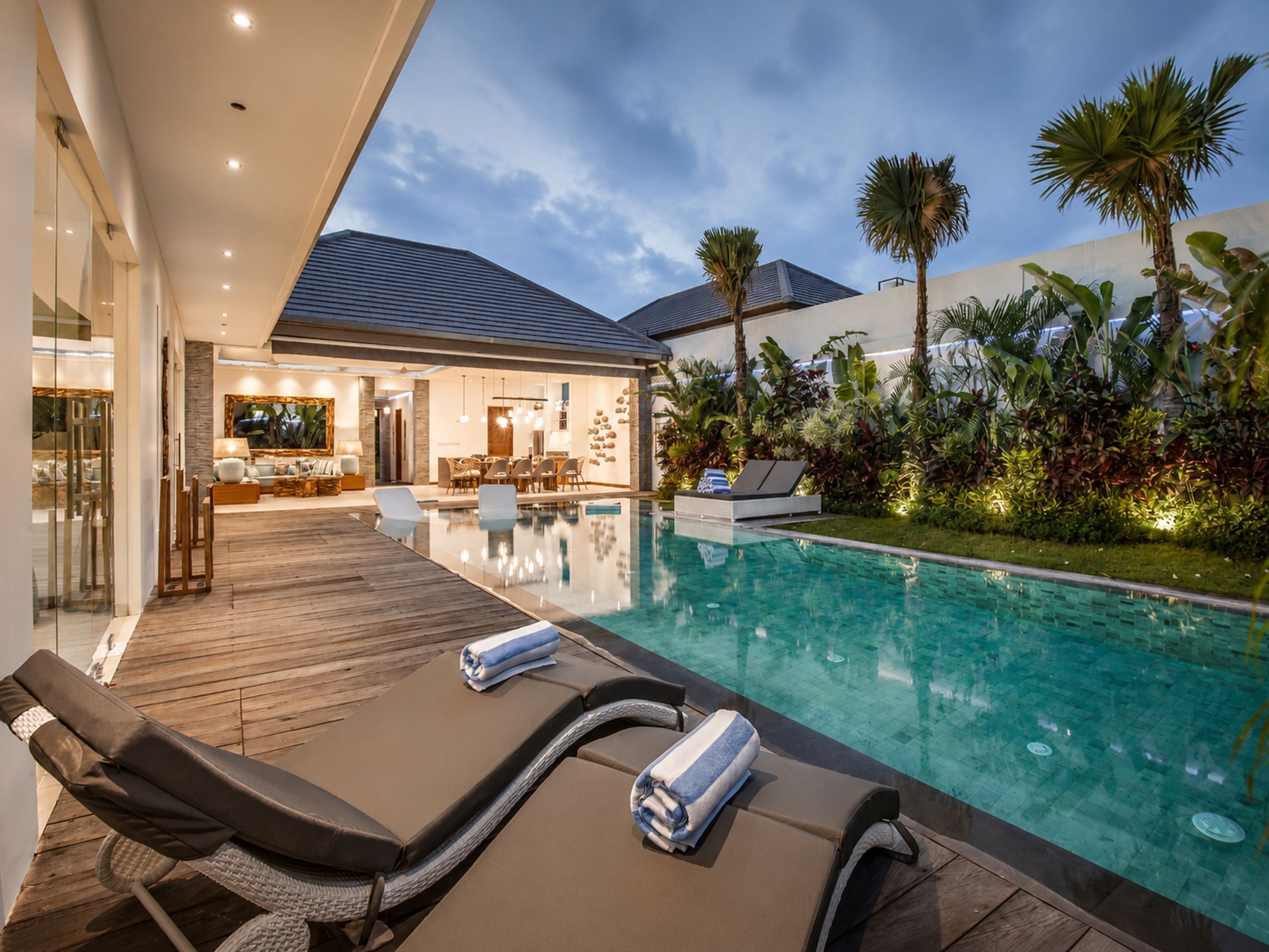 Un espace piscine moderne avec des chaises longues et un coin repas visible au fond.