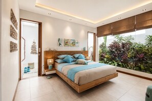 A modern bedroom with a wooden bed, bedside lamps, and a view of lush greenery. - Marina Villa in Seminyak (Seminyak)
