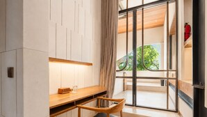 A modern room with a wooden desk and chair, a window with a view of greenery, and a fire extinguisher on the wall. - BAZ Villa 13 Studio 3 Opulent 1-br Loft With Art Deco Shared Pool (Pererenan)