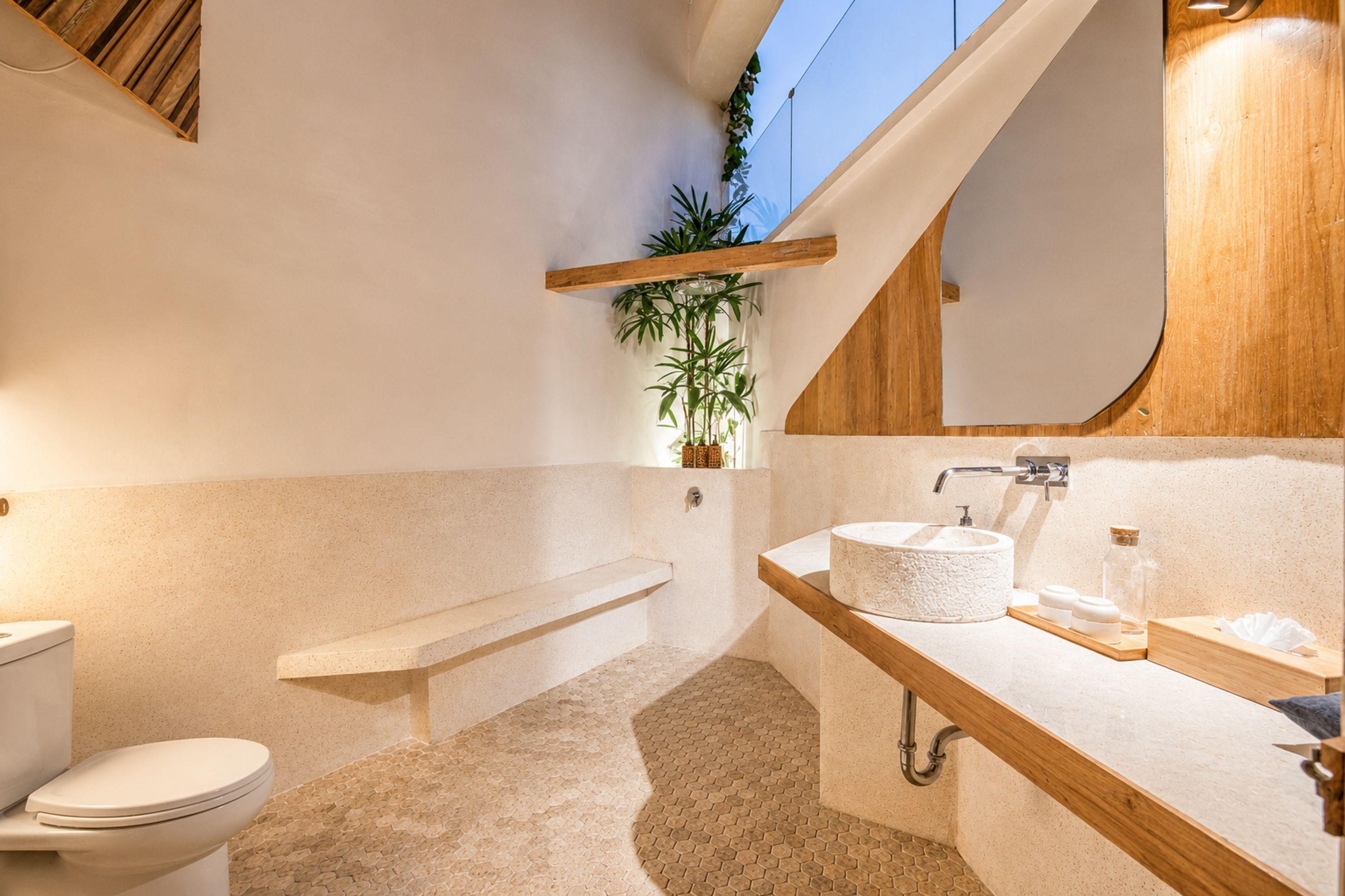 A modern bathroom with a toilet, a bench, a sink with a round basin, and a mirror.