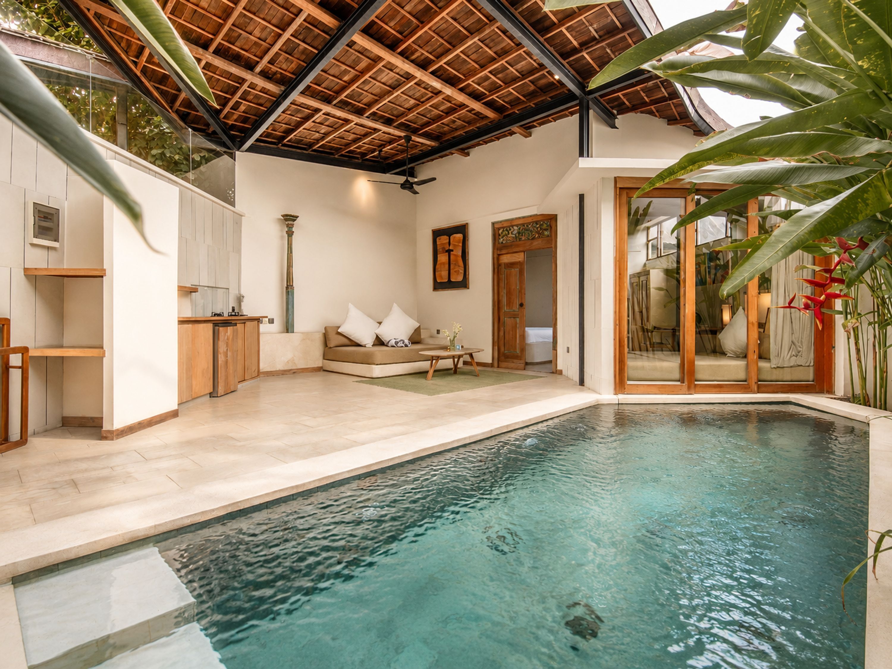 A modern indoor swimming pool with a wooden ceiling, a sofa, and a dining area.