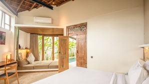 A bedroom with a bed, a desk, and a view of an outdoor area with plants. - BA Villa 2 1BR Elegant 1-br Villa With Pool 800m to Echo Beach (Canggu)