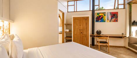A bedroom with a bed, a desk, a chair, a wardrobe, and a window with artwork.