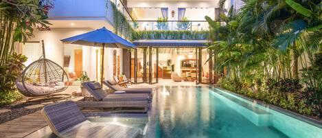 A modern house with a swimming pool, lounge chairs, and a hanging chair.