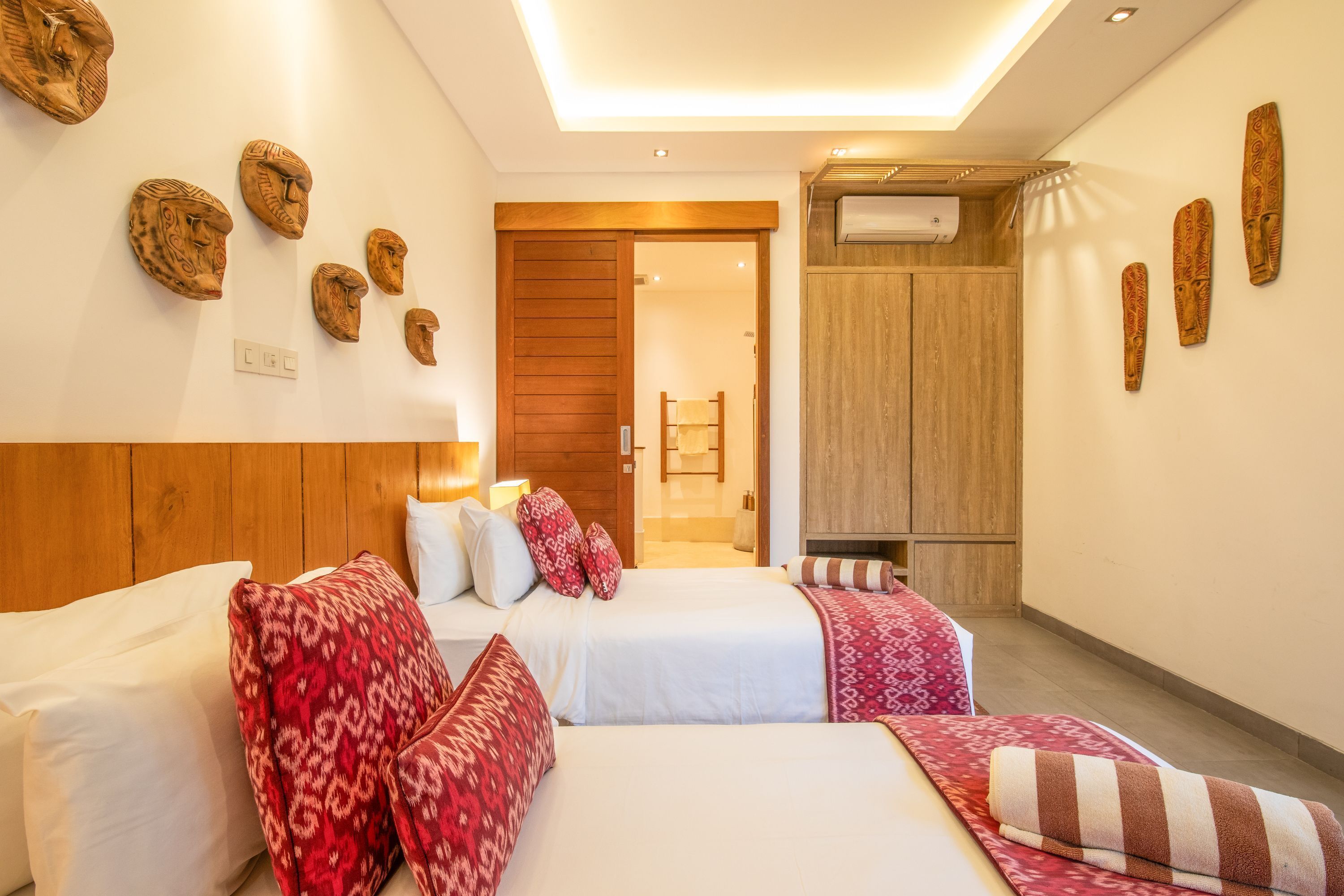 A hotel room with two beds, patterned pillows, a wooden headboard, and wall-mounted decorative items.