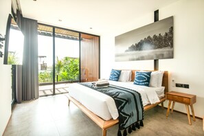 A modern bedroom with a large bed, a wooden nightstand, and a sliding glass door leading to a balcony with greenery.