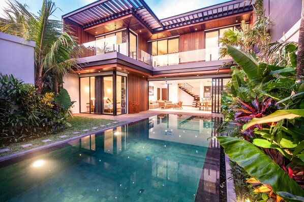 A modern two-story house with a swimming pool, large windows, and a well-maintained garden.