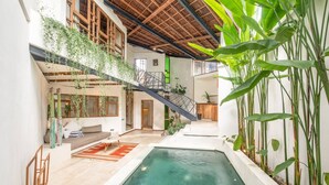 Una piscina interior con una escalera que lleva a un balcón, rodeada de plantas y vigas de madera.