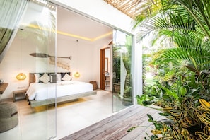 A modern bedroom with a glass door leading to a balcony, a bed with white linens, and a wooden floor. - Canggu Julia 2 in Dalung (Tibubeneng)