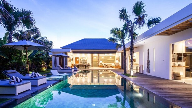 A modern house with a swimming pool, lounge chairs, and a well-lit interior. - Canggu Julia 2 in Dalung (Canggu)