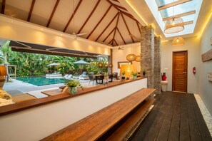 A poolside area with a wooden bench, lounge chairs, and umbrellas. - Canggu Julia 2 in Dalung (Tibubeneng)