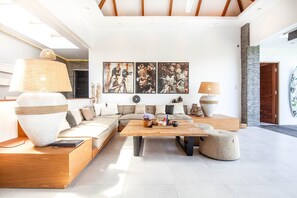 A modern living room with a sectional sofa, a wooden coffee table, and a large vase. There are three framed artworks on the wall and a surfboard leaning against the wall. - Canggu Julia 2 in Dalung (Tibubeneng)