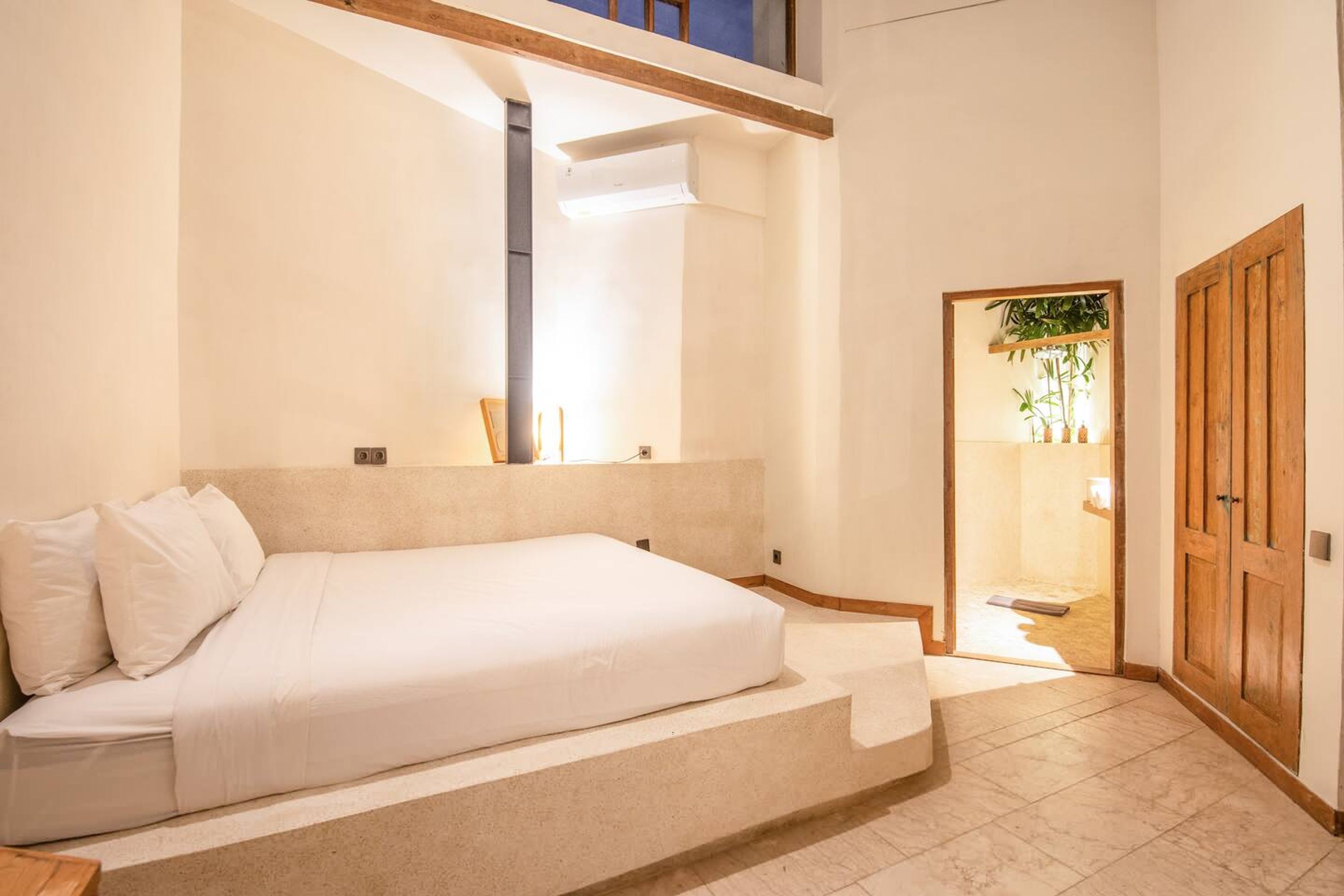 Une chambre à coucher avec un lit, une porte en bois et une petite plante dans un coin.