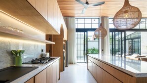 A modern kitchen with wooden cabinetry, a central island, and pendant lighting. - Villa Serai 5br to the Beach (Pecatu)