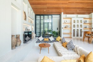 A modern living room with a sofa, coffee table, and shelves with decorative items. - Villa Serai 5br to the Beach (Pecatu)