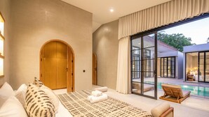 A bedroom with a large bed, a wooden wardrobe, and a view of a swimming pool. - Villa Serai 5br to the Beach (Pecatu)