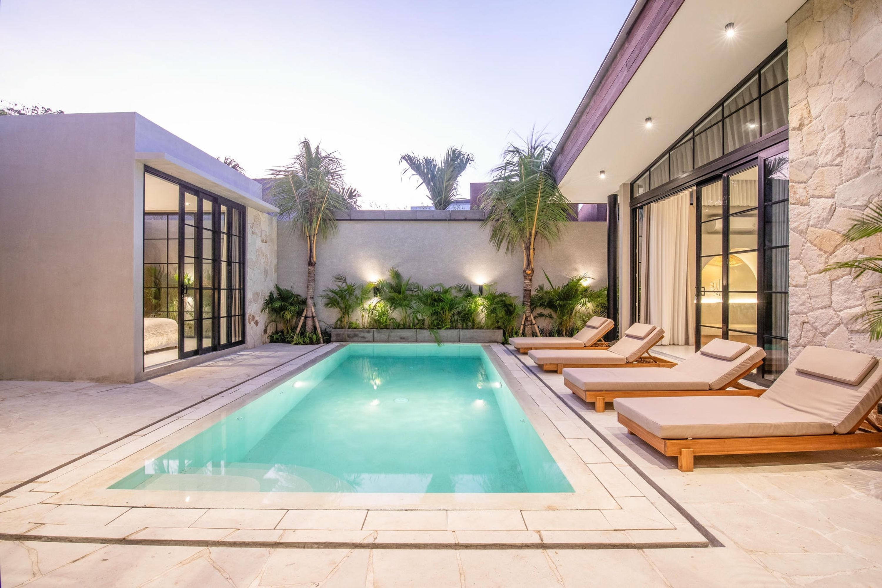 A modern outdoor pool area with a clear pool, lounge chairs, and a stone wall.