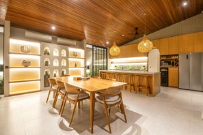 A modern kitchen with wooden cabinets, a central island with bar stools, and pendant lighting. - Villa Serai 5br to the Beach (Pecatu)