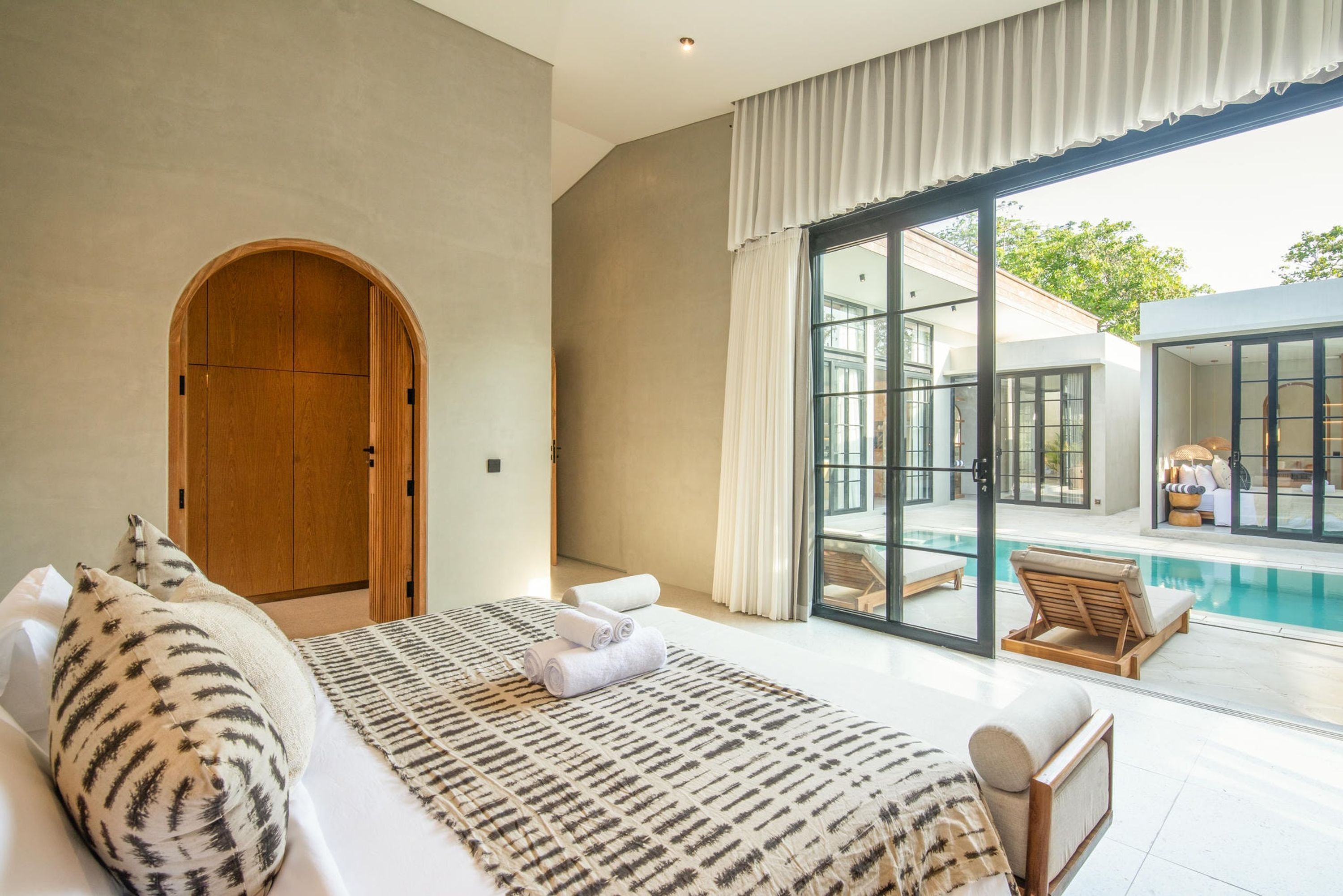 A bedroom with a large bed, a wooden wardrobe, and a view of a swimming pool.