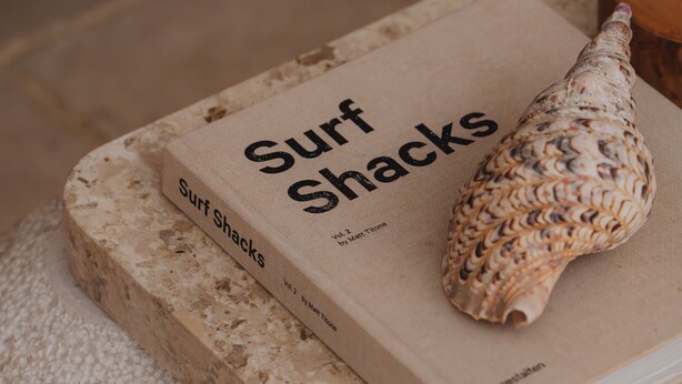 A book titled 'Surf Shacks' on a textured surface with a seashell. - Xanthe 3BR Villas 2 Mins to Ulu Beach (Pecatu)