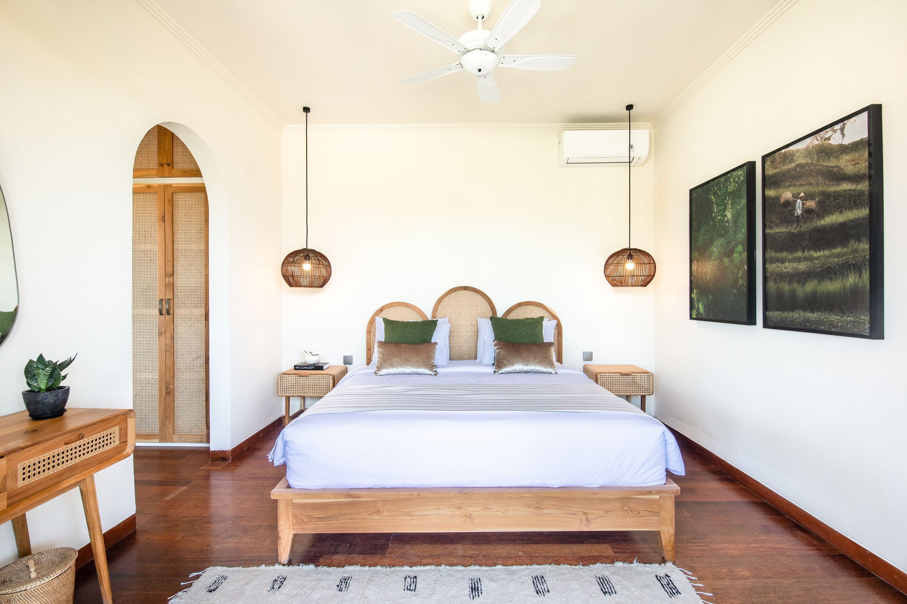 A bedroom with a large bed, wooden headboard, two bedside tables with lamps, a ceiling fan, and two framed pictures on the wall.