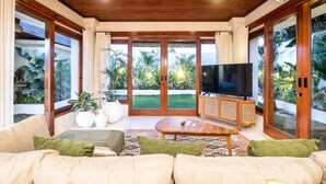Ein geräumiges Wohnzimmer mit Holzboden, großen Schiebegläsern zum Garten hin, einem Flachbildfernseher und einem bequemen Sofa.