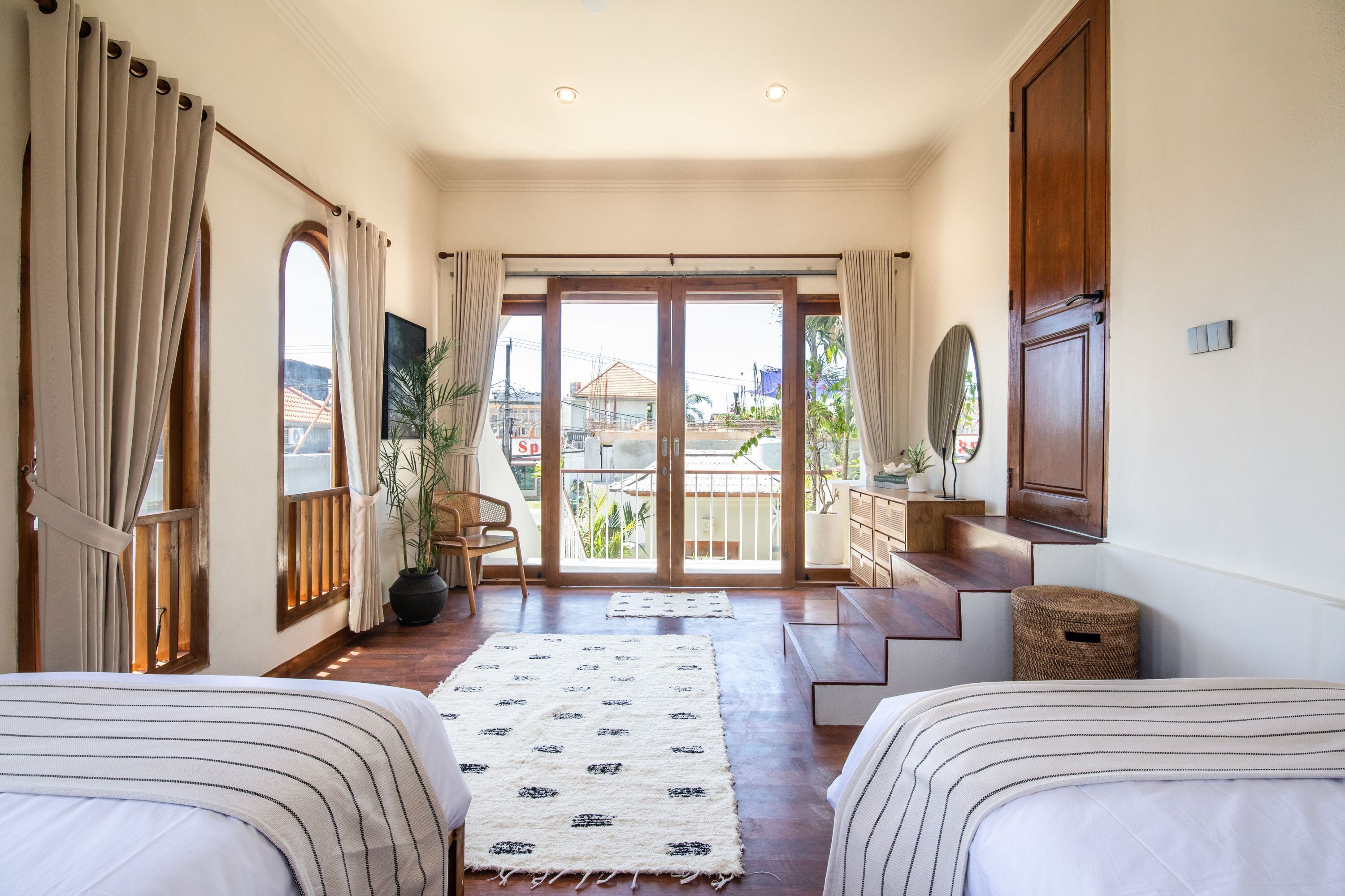 A hotel room with a large sliding glass door leading to a balcony, a bed with striped bedding, a small desk, and a potted plant.