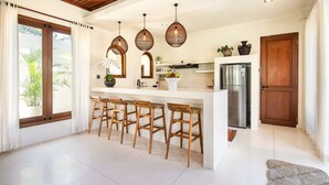 Eine moderne Küche mit einer zentralen Kochinsel, Holzhocker, hängenden Korbstühlen und einem Edelstahl-Kühlschrank.